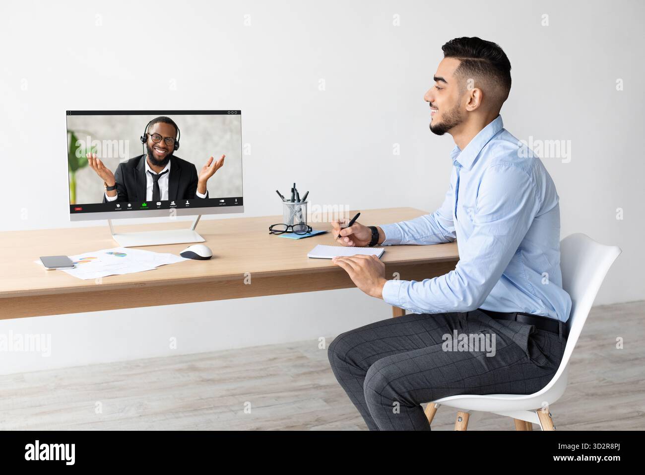 Junger arabischer Mann bei Videoanruf während der Arbeit am Schreibtisch in moderner Büroumgebung Stockfoto