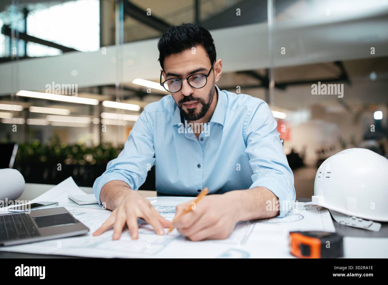 Techniker arbeitet tagsüber an detaillierten Plänen in einem modernen Büroumfeld Stockfoto