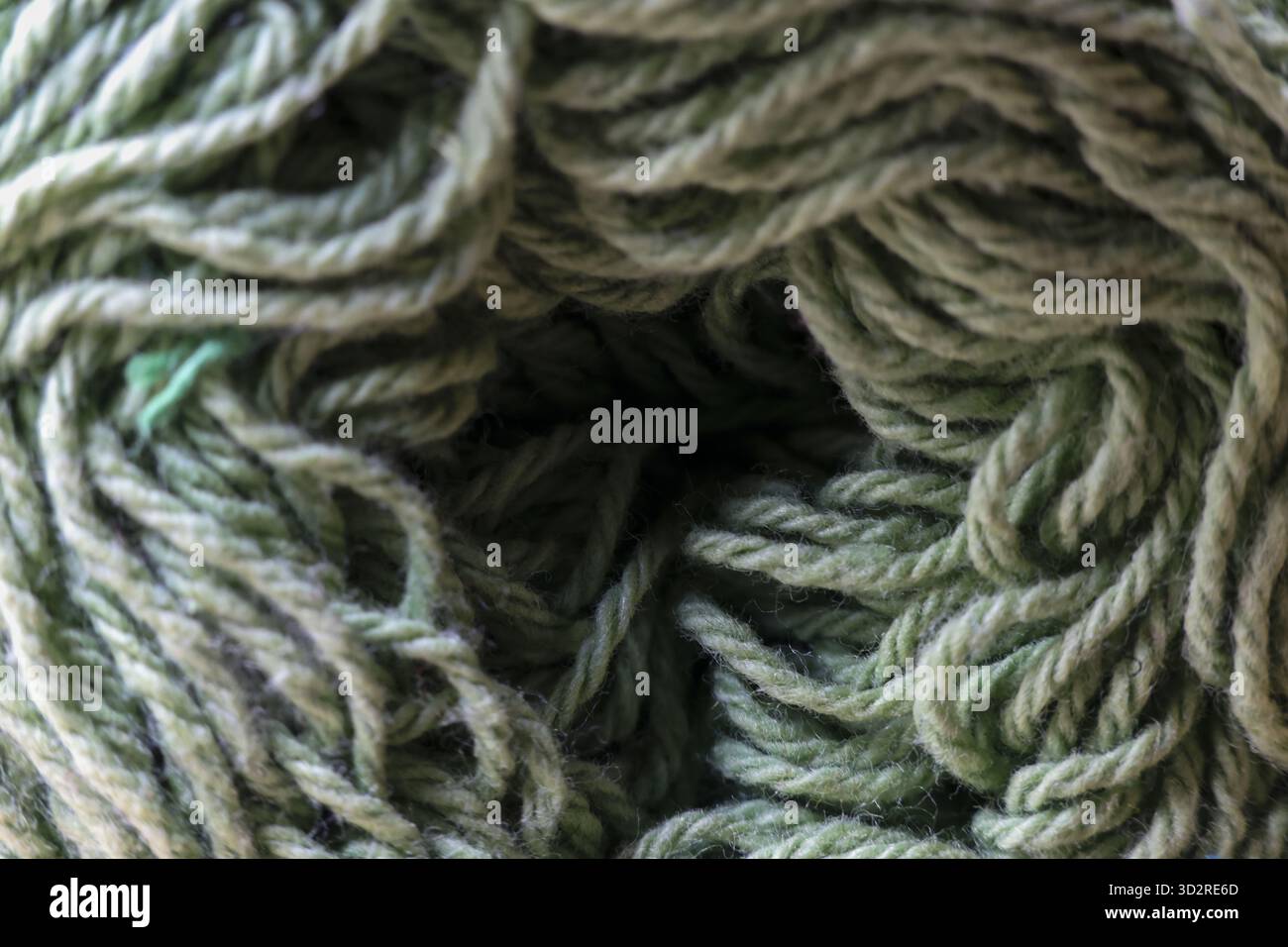 Gemütlicher Makrohintergrund aus weichem grünem Garn. Wollkugel zum Stricken oder Häkeln. Handgefertigtes Material, das ein Gefühl von Wärme und Kreativität vermittelt Stockfoto