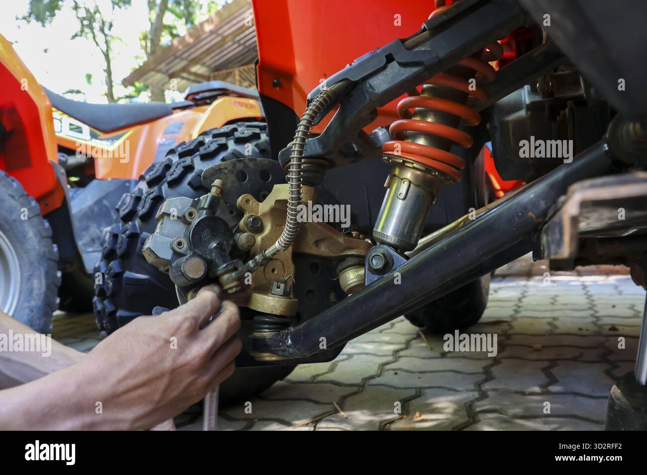 Fokussierte Mechaniker, die Fahrzeugreparaturen auf dem roten Quad durchführen. Man fixiert Federung und Stoßdämpfer mit Werkzeug, konzentriert auf Wartungsservice o Stockfoto