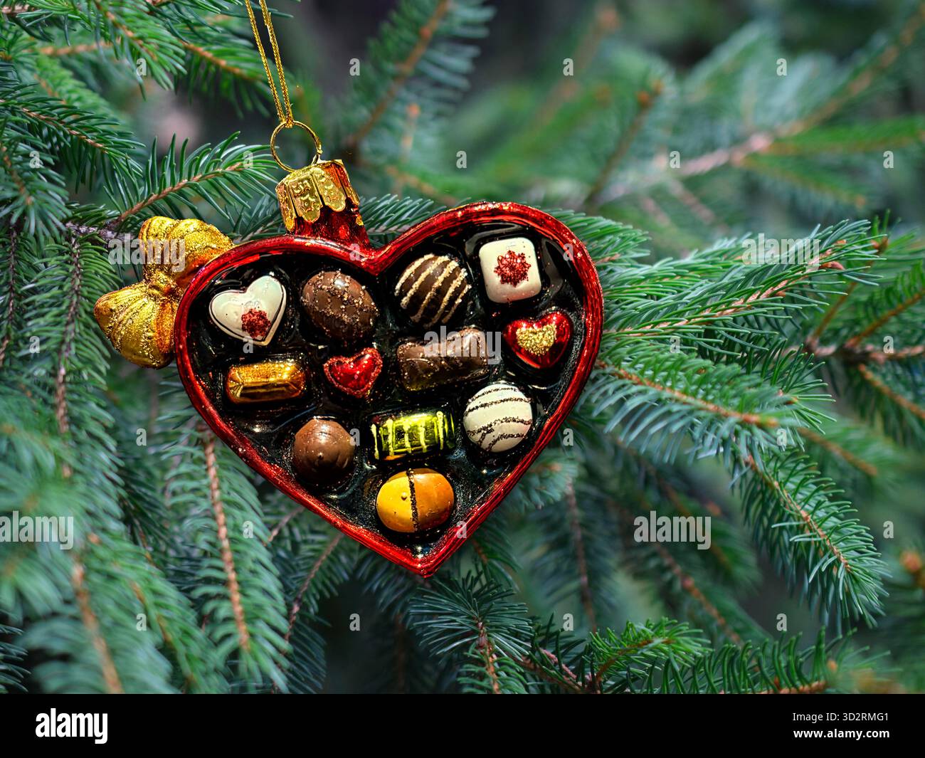 Weihnachtsschmuck in Herzform mit Pralinen im Inneren. Schokoladenbox mit Baumhintergrund. Stockfoto