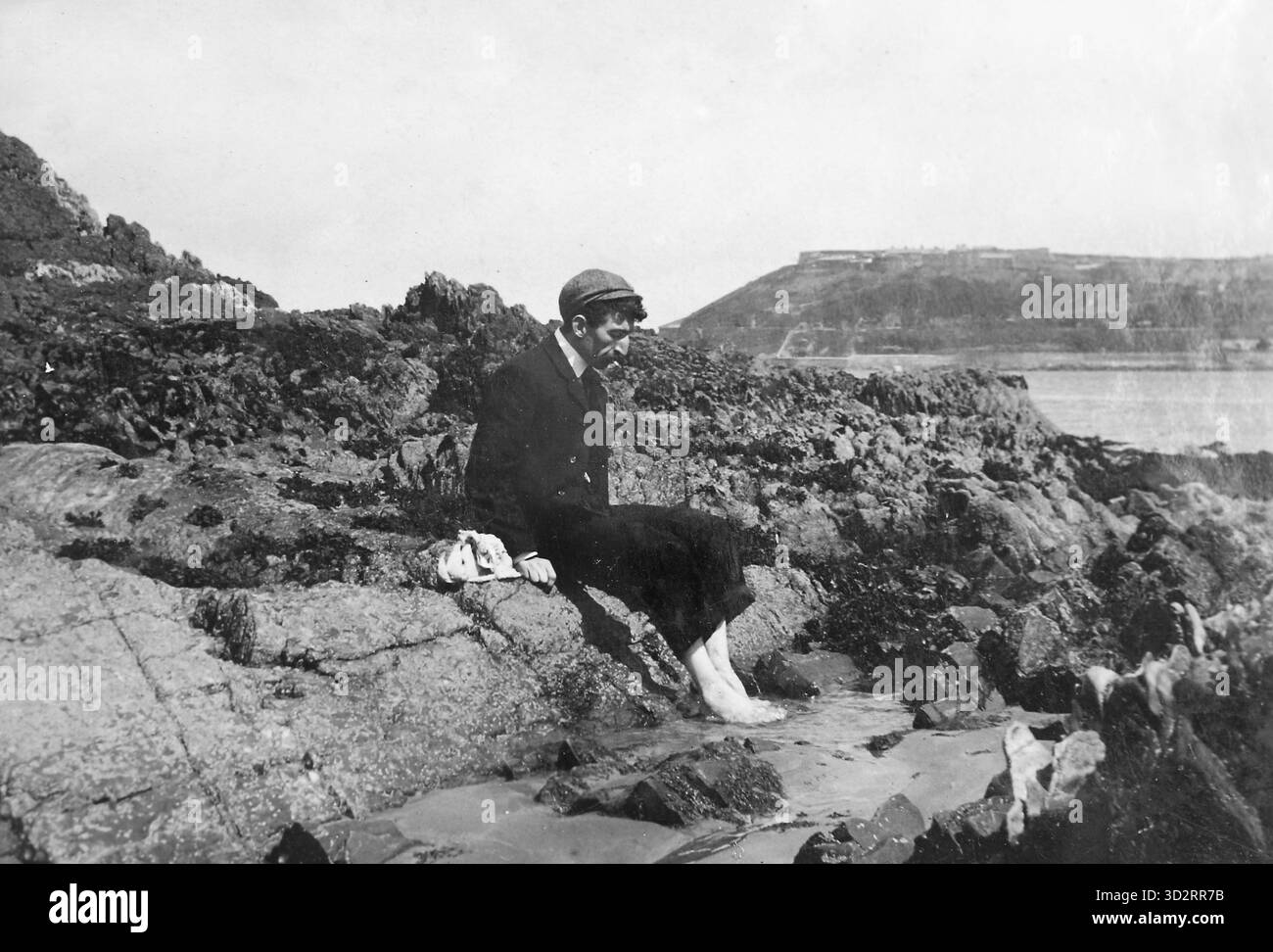 Ein junger Ire sitzt am Meer mit Schuhen und Socken, ca. 1895. Stockfoto