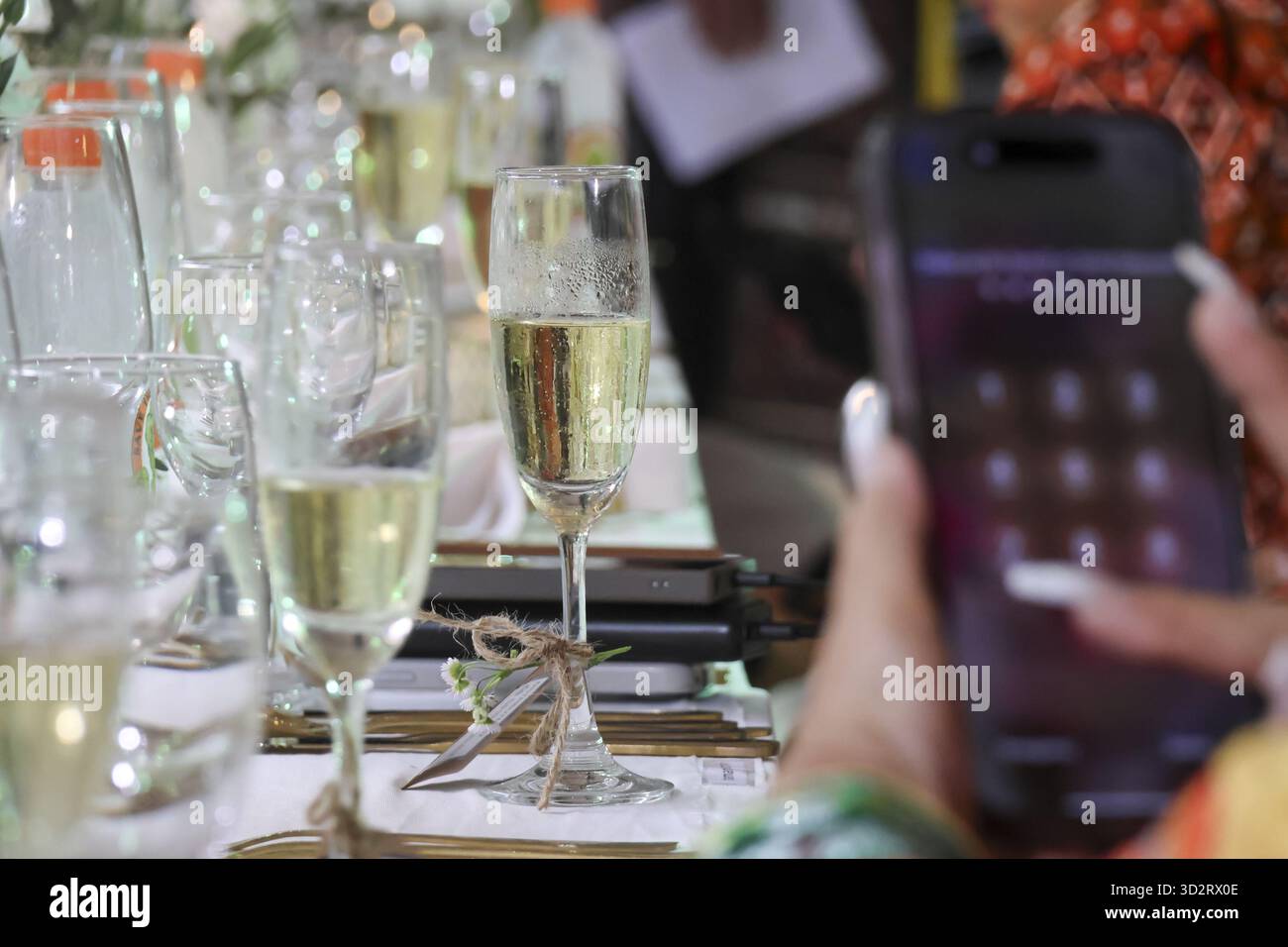 Festliche Feier mit Sektgläsern und Person, die das Smartphone nutzt, hält Momente der Freude und Verbindung bei geselligen Treffen fest, mit Vorfreude Stockfoto