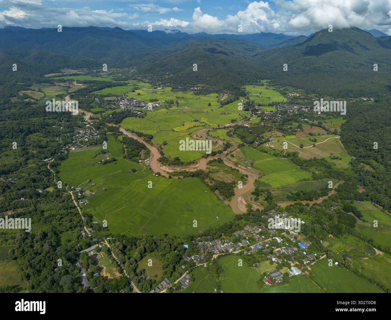 Panoramablick aus der Luft, üppige grüne Landschaft. Der sich windende braune Fluss fließt durch ein riesiges fruchtbares Tal. Abgelegenes Dorf eingebettet in grüne Natur. Outdo Stockfoto