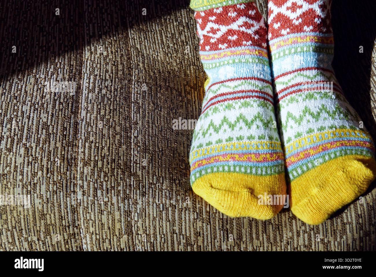 Füße in leuchtenden, mehrfarbigen Socken, die auf einer Couch liegen. Symbolisiert den Stil der Homewear, die nordische Stricktradition und die Lifestyle-Ästhetik von Hygge. Stockfoto
