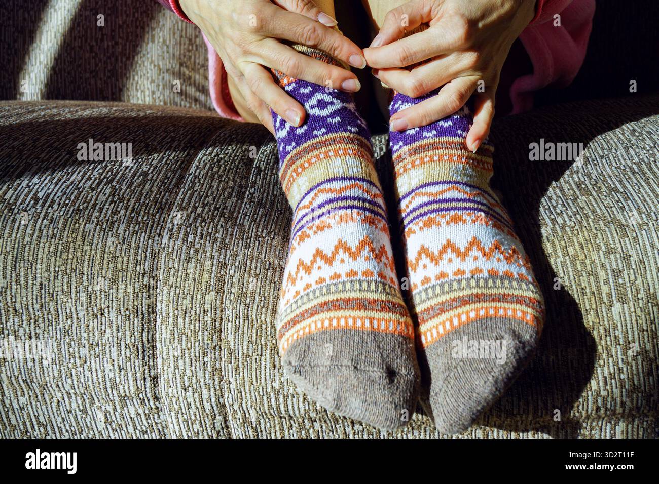 Entspannte Füße in farbenfrohen, geometrisch gemusterten Socken, die Hände berühren sanft die Knöchel. Steht für Gemütlichkeit zu Hause und den Komfort langsamer Momente. Stockfoto