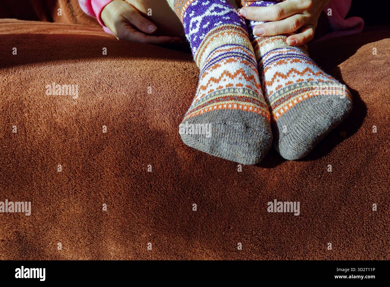 Eine Person, die auf einem Sofa ruht und bunte gemusterte Socken trägt. Symbolisiert Entspannung zu Hause, gemütliche Kleidung, Wochenendleben und Selbstpflegemoment. Stockfoto