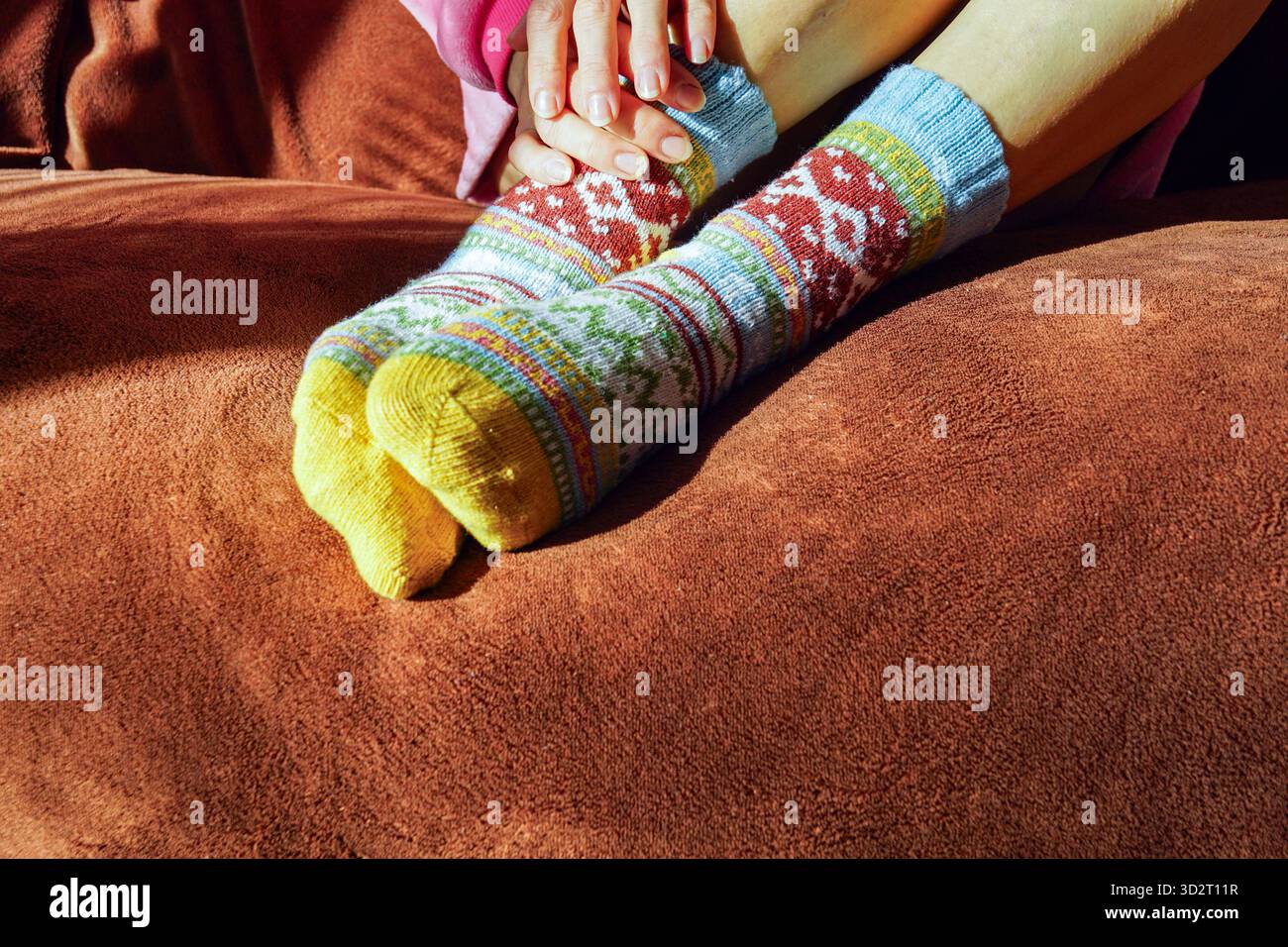 Die Füße einer Frau tragen farbenfrohe Socken mit Norwegermuster, während sie auf einer Decke liegen. Symbolisiert Wärme und gemütliche ästhetische Wertschätzung. Stockfoto