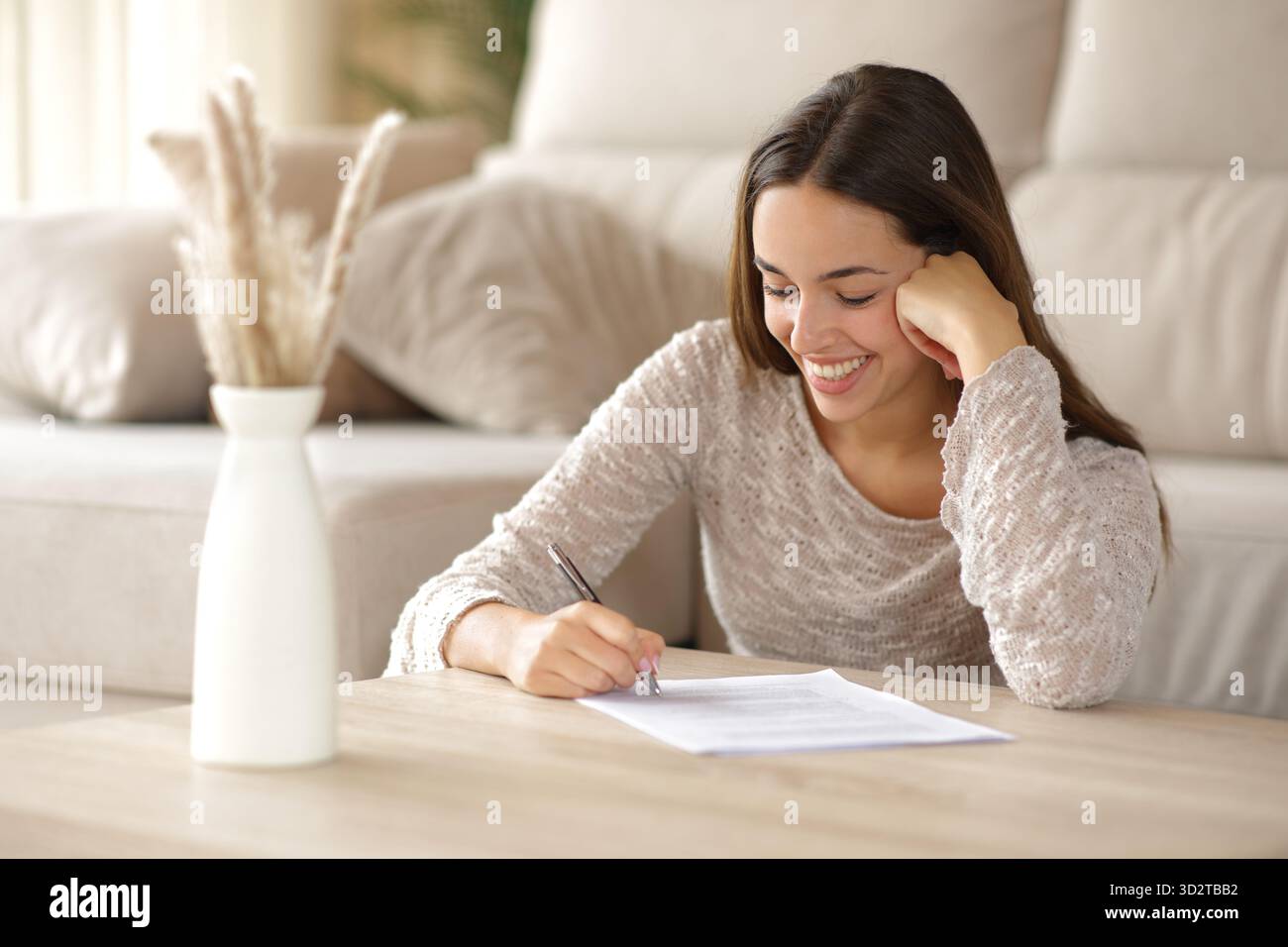 Glückliche Frau unterschreibt Papierformular auf einem Couchtisch zu Hause Stockfoto