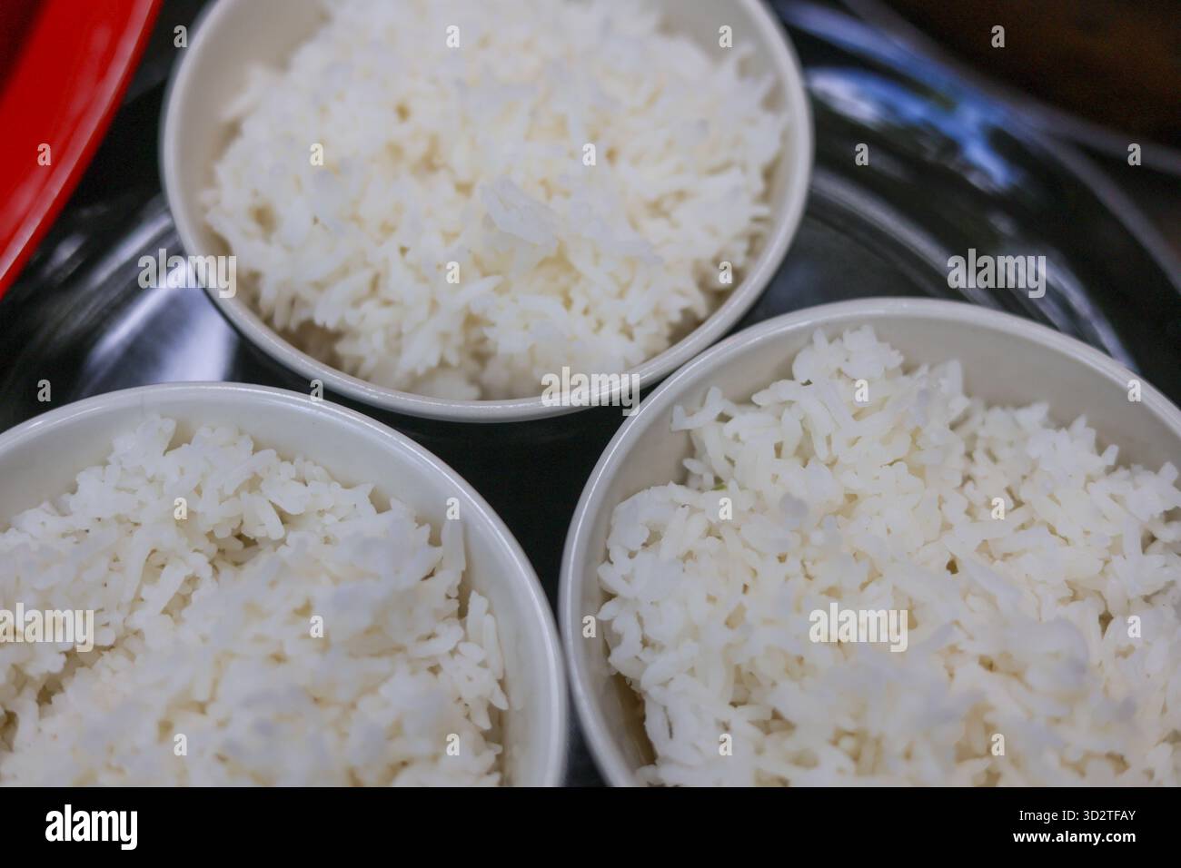 Nahaufnahme von oben auf drei einfache weiße Schüssel mit flauschigem gekochtem Reis. Warmer Dampfgarteil der Grundgetreidemahlzeit, die verzehrfertig ist, steht für Wohlbefinden Stockfoto