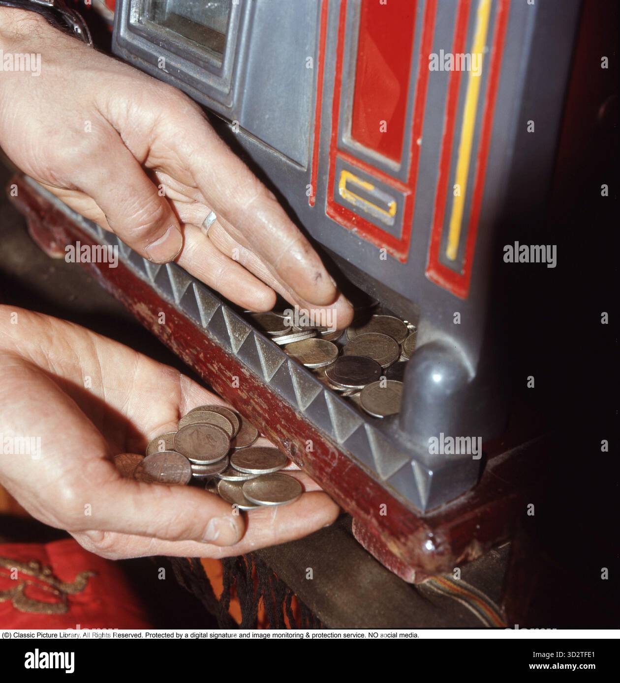 Am Spielautomaten 1972. Eine Person, die am Spielautomaten abgebildet ist. Ein Spielautomat, in dem man eine Münze einsteckt und einen Hebel zieht, der das Drehen von drei Rädern beginnt. Sobald sie anhalten und die Räder dasselbe Symbol zeigen, gewinnen Sie. Der einarmige Bandit, ein klassischer Spielautomat, entstand Ende des 19. Jahrhunderts, als Charles Fey’s Liberty Bell 1895 Pionier war. Benannt nach seinem Einzelhebel, den die Spieler ziehen, um die Walzen zu drehen, wurde es zu einem Grundnahrungsmittel für das Casino. In den 1950er Jahren waren diese Maschinen mit bunten Symbolen wie Früchten und Glocken ausgestattet, die Geldpreise für passende Kombinationen boten. Die Stockfoto