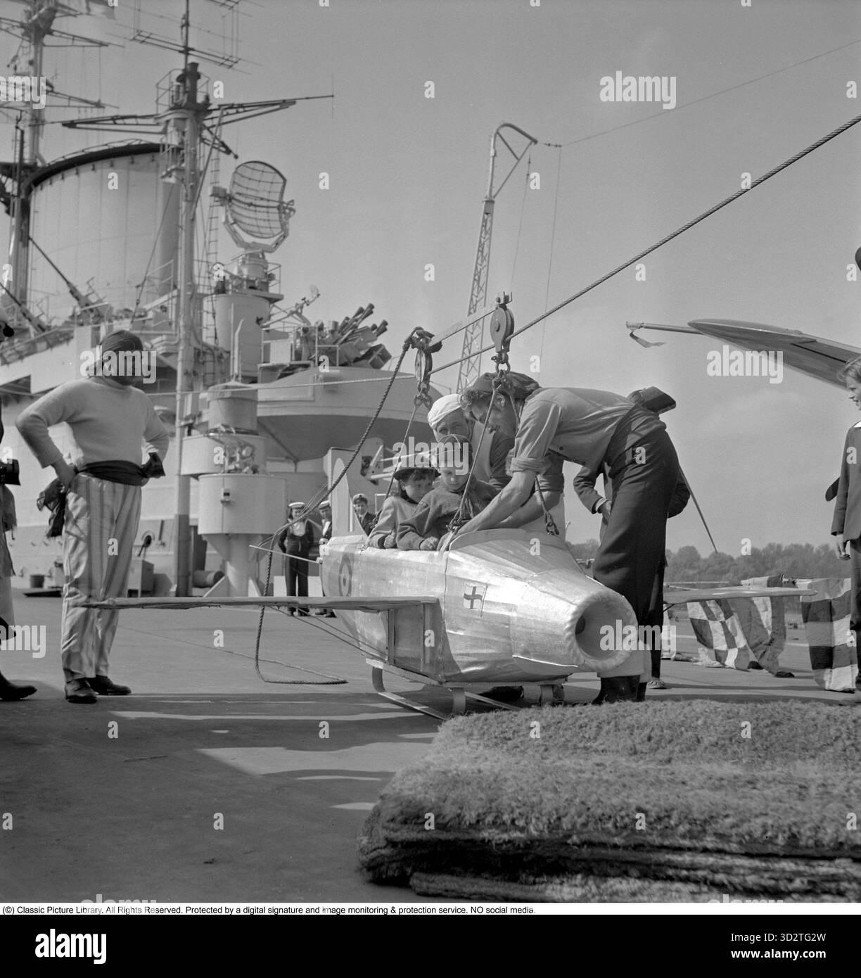 Britischer Marinebesuch, 1951. Kinderparty und aufregende Aktivitäten an Bord des britischen Flugzeugträgers HMS Indomitable während seines Besuchs in Stadsgårdshamnen, Stockholm. Das Fliegen in einem Modell eines Militärflugzeugs ist eine beliebte Aktivität. HMS Indomitable war ein Flugzeugträger der Royal Navy, der 1940 gestartet wurde und während des Zweiten Weltkriegs und der Nachkriegszeit aktiv war. Im Juni 1951 besuchte das Schiff Stockholm im Rahmen einer Goodwill-Tour der British Home Fleet. Admiral Sir Philip Vian, Oberbefehlshaber der Heimatflotte, flog während des Besuchs seine Flagge an Bord von Indomitable. Das Schiff hat in Stadsgårdsha angedockt Stockfoto