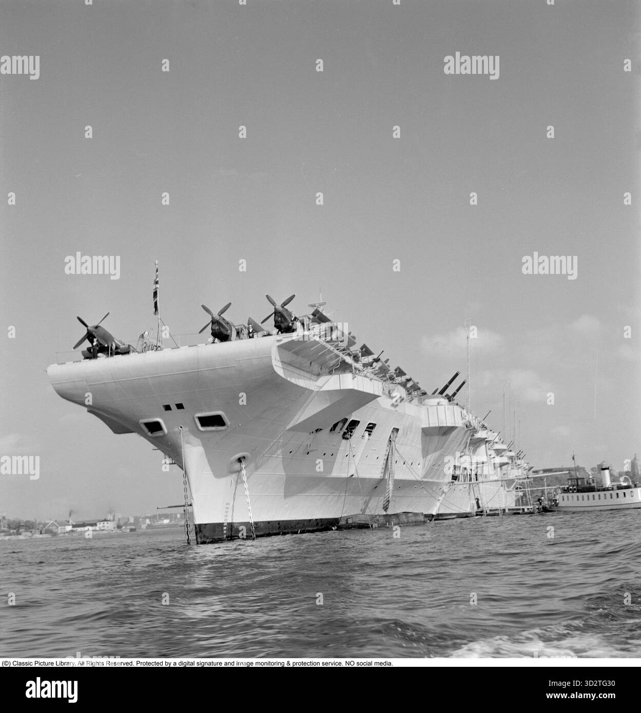 Britischer Marinebesuch, 1951. Der britische Flugzeugträger HMS Indomitable während seines Besuchs in Stadsgårdshamnen, Stockholm. HMS Indomitable war ein Flugzeugträger der Royal Navy, der 1940 gestartet wurde und während des Zweiten Weltkriegs und der Nachkriegszeit aktiv war. Im Juni 1951 besuchte das Schiff Stockholm im Rahmen einer Goodwill-Tour der British Home Fleet. Admiral Sir Philip Vian, Oberbefehlshaber der Heimatflotte, flog während des Besuchs seine Flagge an Bord von Indomitable. Das Schiff legte in Stadsgårdshamnen an, wo es zum Mittelpunkt der Aufmerksamkeit wurde. Schwedische Würdenträger, darunter König Gustaf VI. Adolf, inspizierten die Stockfoto