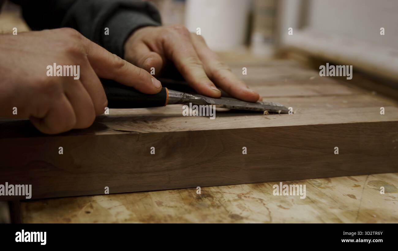 Handwerkliche Hände meißeln sorgfältig dunkles Holz für ein feines Finish Stockfoto