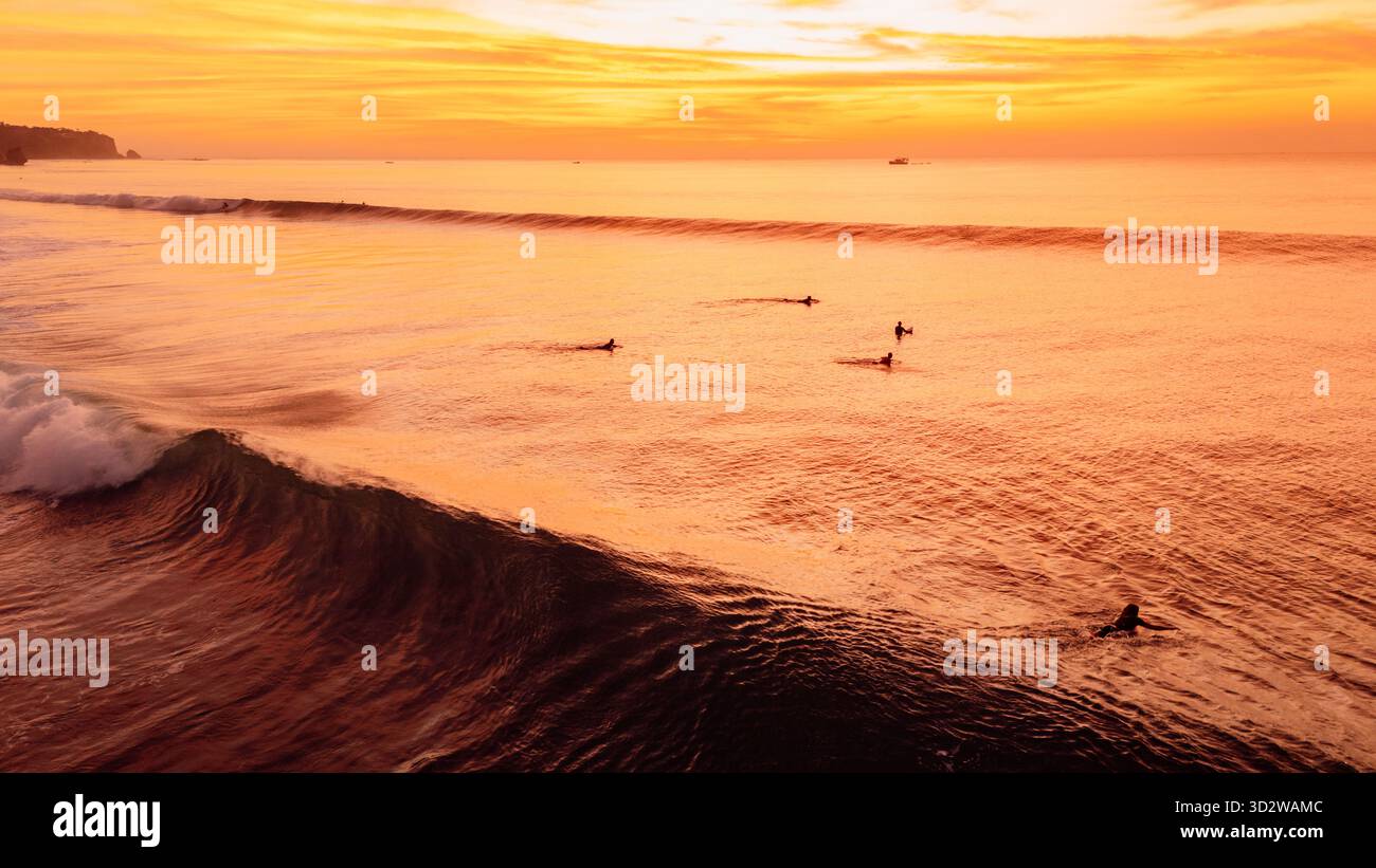 Goldener Sonnenuntergang über Meereswellen mit Surfern und hellem Himmel Stockfoto