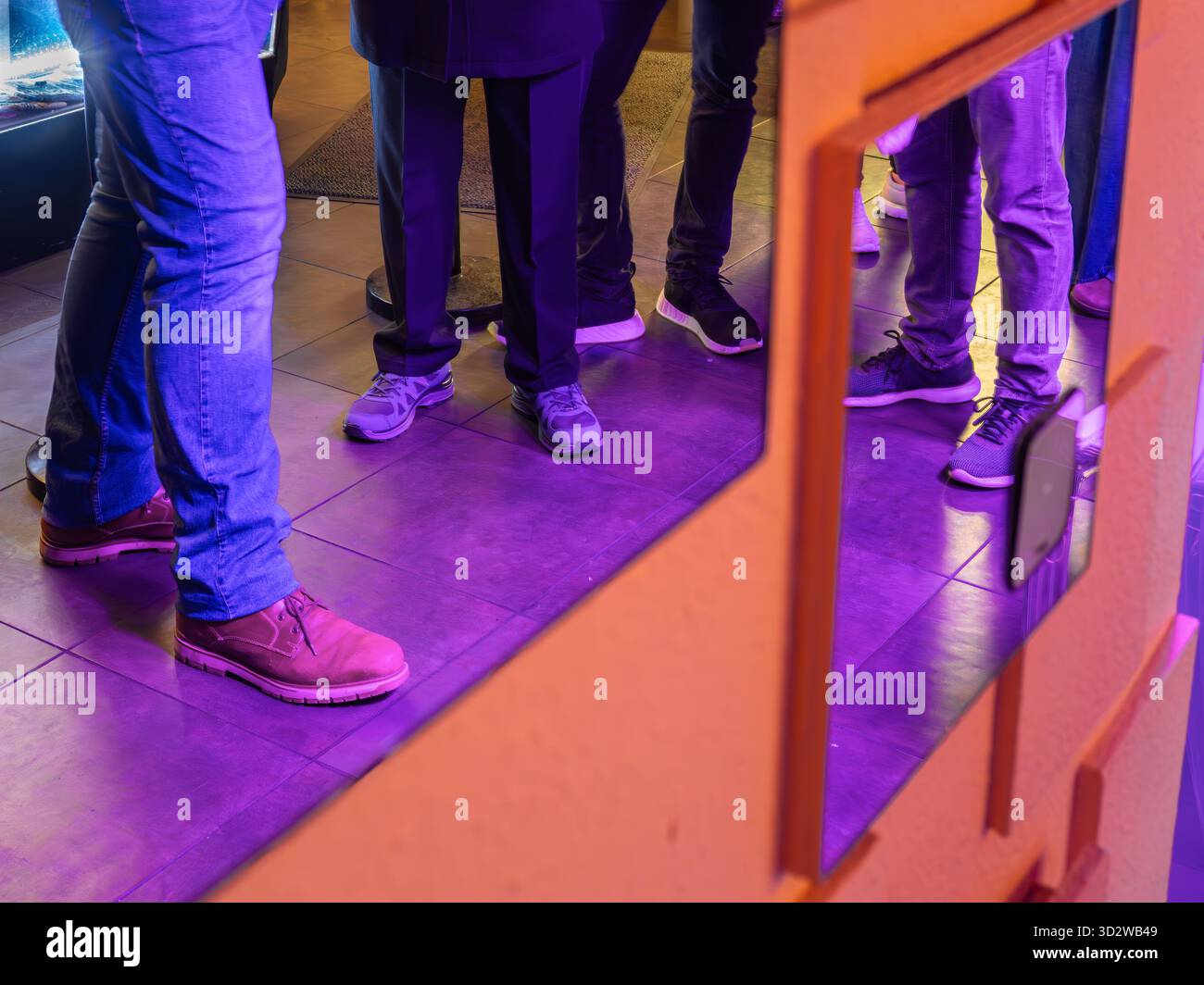 Beine und Schuhe von Menschen in einem Raum mit violetter Beleuchtung. Stockfoto