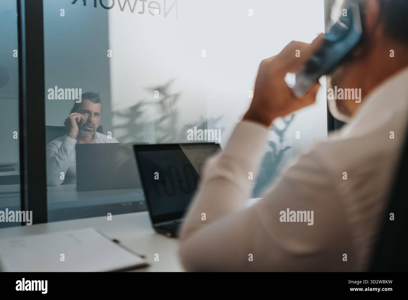 Geschäftsmann telefoniert in einem modernen Büro mit Laptop und Glaswand Stockfoto