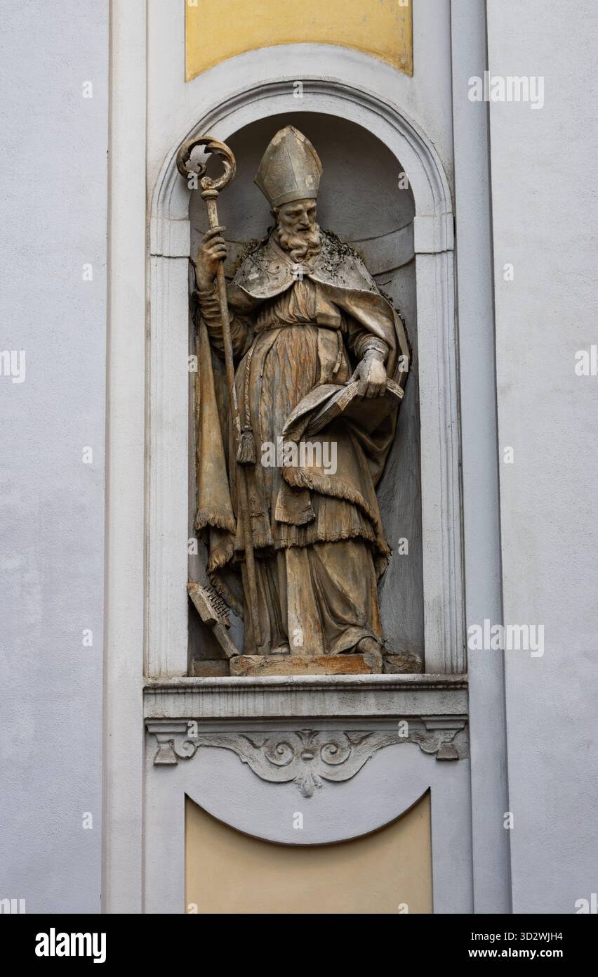 Die Steinstatue des Bischofs steht in einer reich verzierten Wandnische, die das katholische Erbe und die italienische religiöse Architektur mit symbolischen heiligen Details darstellt. Stockfoto