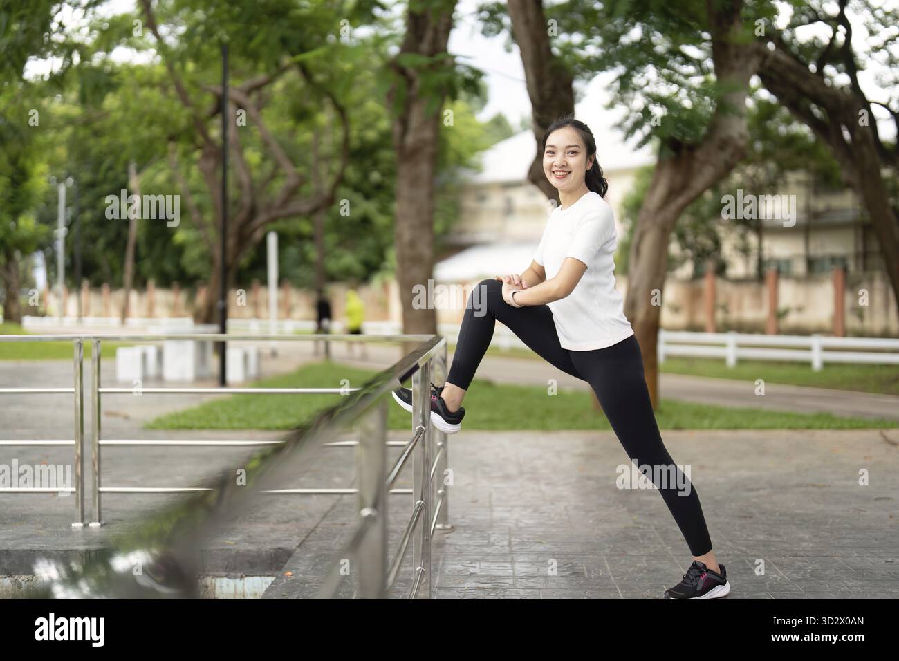 Eine Frau streckt ihr Bein auf einem Geländer in einem Park und zeigt Selbstvertrauen und Fitness. Highlights des aktiven Lebensstils und Wellness im Freien Stockfoto