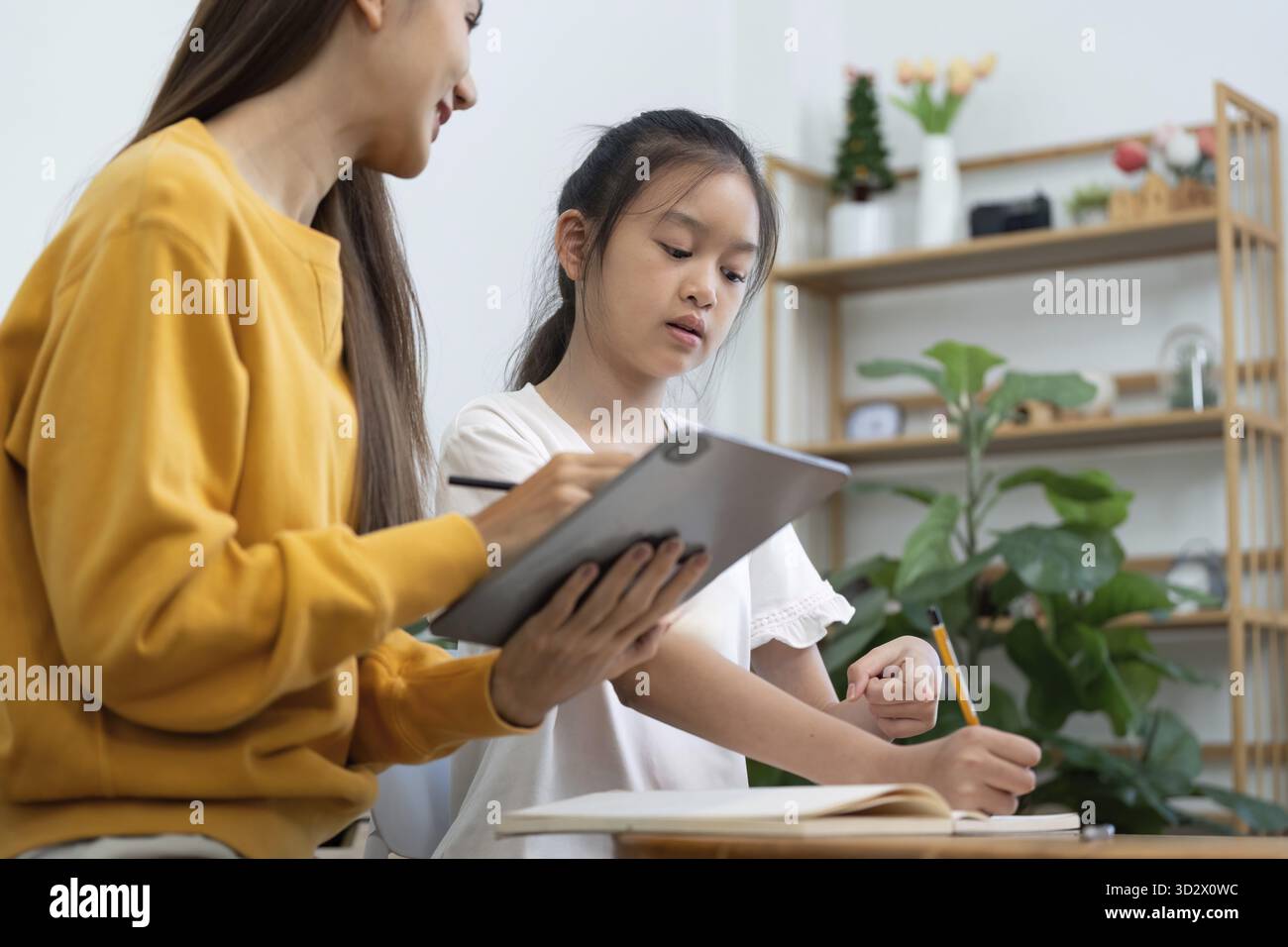 Eine Mutter und Tochter nehmen zu Hause Lernaufgaben wahr und betonen den Spaß und die Unterstützung während ihrer Schulvorbereitungen Stockfoto