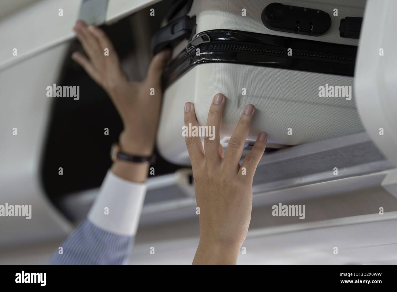 Ein fokussierter Reisender verstaut ihr Gepäck im Gepäckraum, während er in das Flugzeug einsteigt, um ihre Sachen effizient zu verwalten Stockfoto