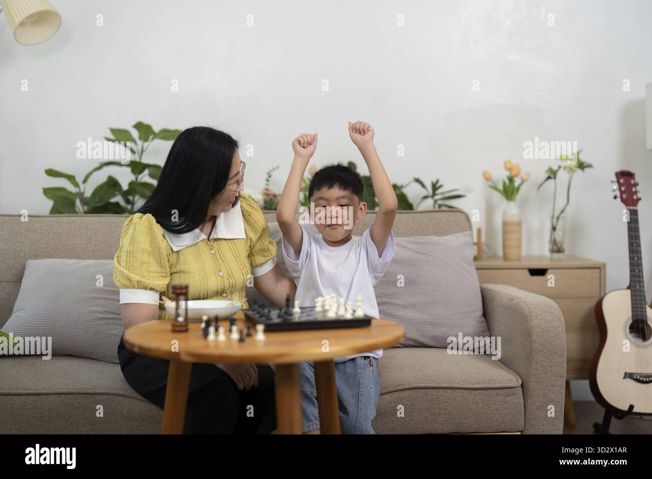 Ein stolzer Moment, in dem ein Sohn ein Schachspiel mit seiner Mutter gewinnt, um Freude und gemeinsame Erfahrungen im Familienleben zu zeigen Stockfoto