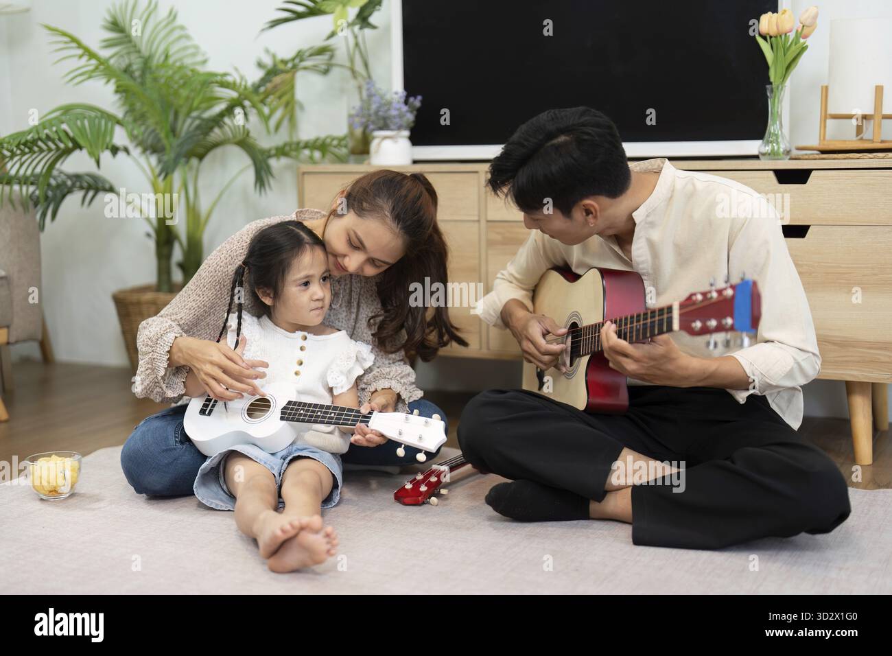 In einer reizvollen Familienszene spielen eine Mutter und ihre Tochter zusammen und fördern Kreativität und Freude durch Musik in einer gemütlichen Umgebung Stockfoto