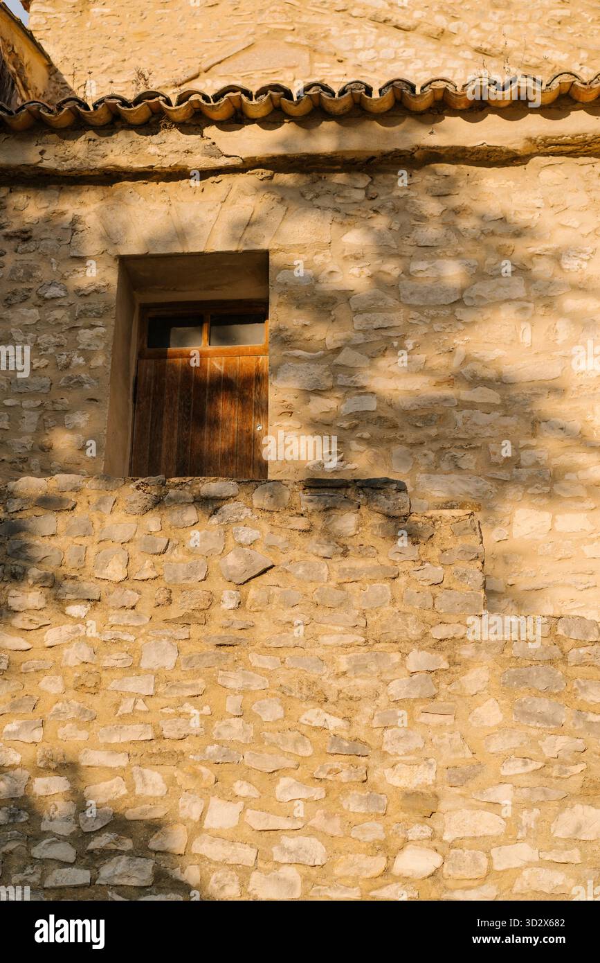 Charmante rustikale Steinhausfassade mit grünen Pflanzen, Fenster mit Holzläden. Künstlerisches Licht und Schatten an der Wand. Gemütliches Landhaus Stockfoto