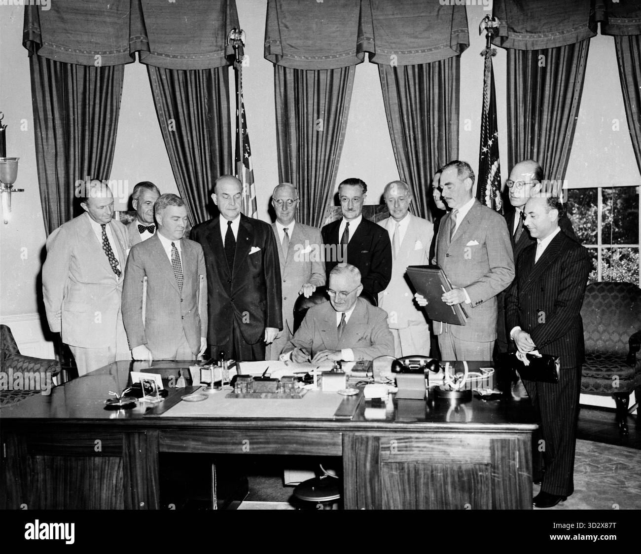 WASHINGTON DC, USA - 24. August 1949 - US-Präsident Harry Truman unterzeichnete das Dokument zur Umsetzung des Nordatlantikvertrags an seinem Schreibtisch im Oval Office des Weißen Hauses in Washington DC, USA, während einige Würdenträger sich das Bild machen. Von links nach rechts: Sir Frederick Hoyer Millar, Chargé d'affaires, Vereinigtes Königreich; Botschafter Henrik de Kauffmann von Dänemark; W D Matthews, Charge d'Affaires, Kanada; Verteidigungsminister Louis A Johnson; Botschafter Wilhelm Munthe de Morgenstierne von Norwegen; Botschafter Henri Bonnet von Frankreich; Baron Robert Silvercruys, Botschafter von Belgien; Botschafter Pedro Teotóni Stockfoto