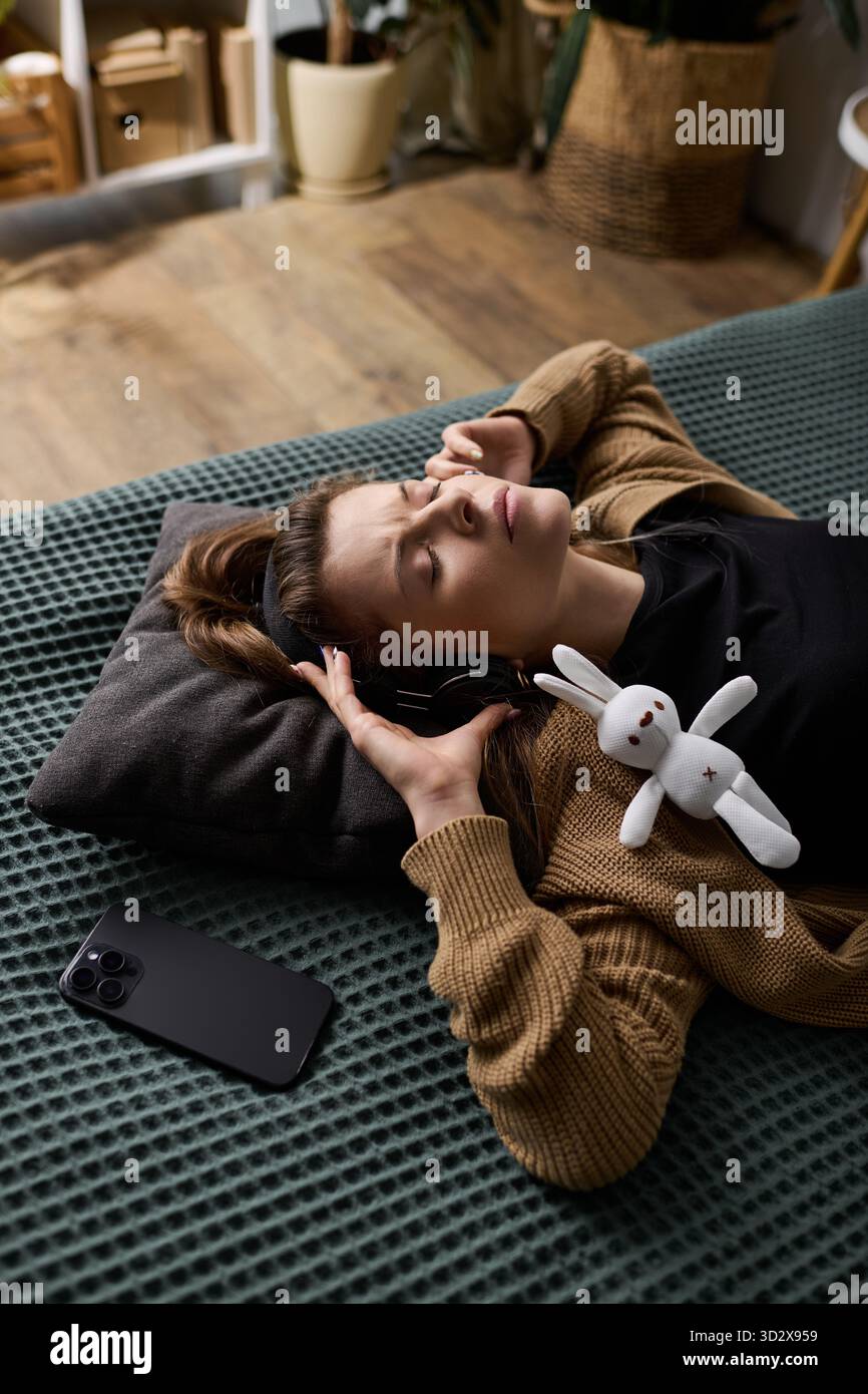 Eine junge Frau entspannt sich in ihrem Bett und genießt Musik, während sie von Komfort und Gelassenheit umgeben ist. Stockfoto