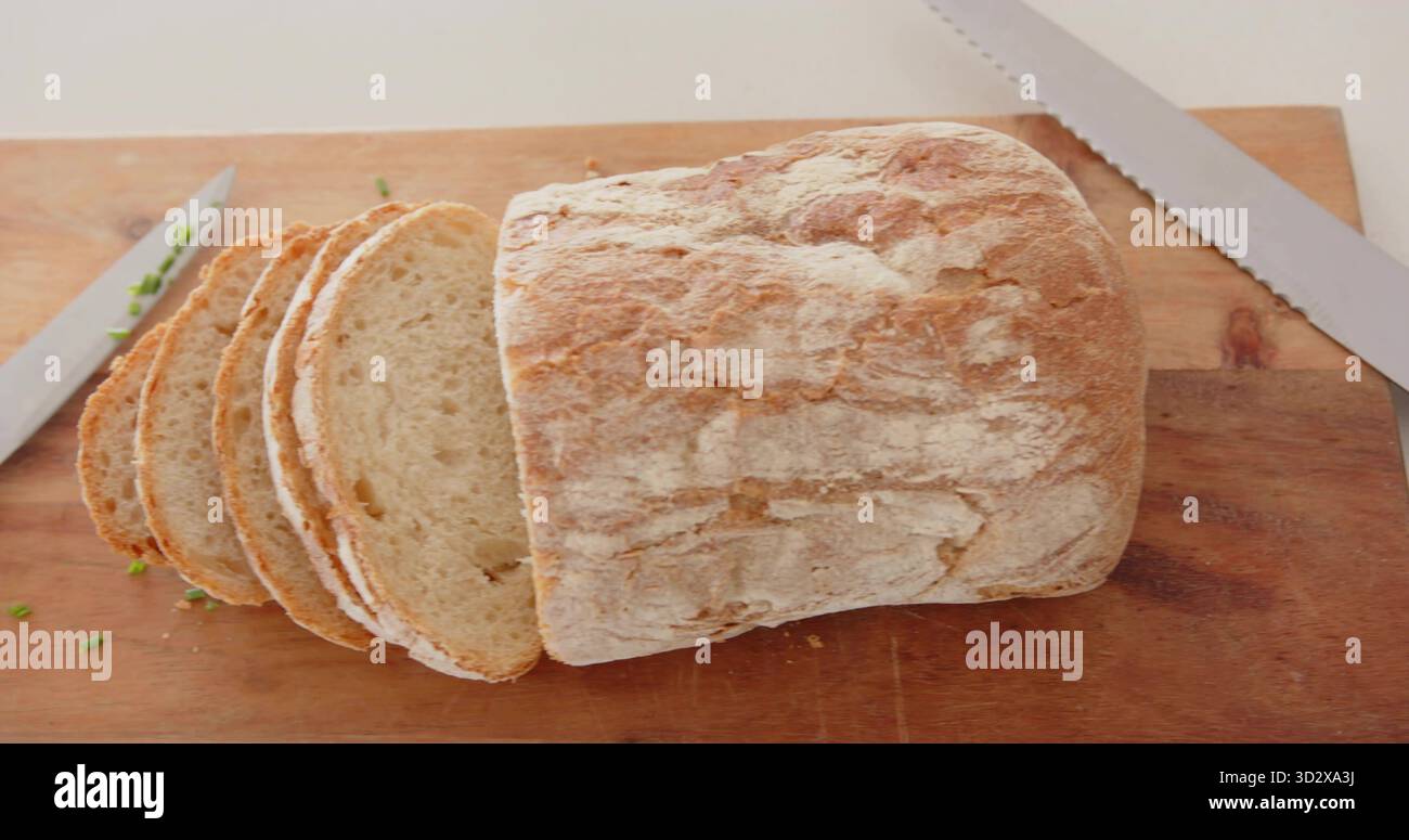 Mit knusprigem handwerklichem Brotbrot, der auf hölzernem Schneidebrett sitzt, mit Messern und Kräuterstückchen Stockfoto