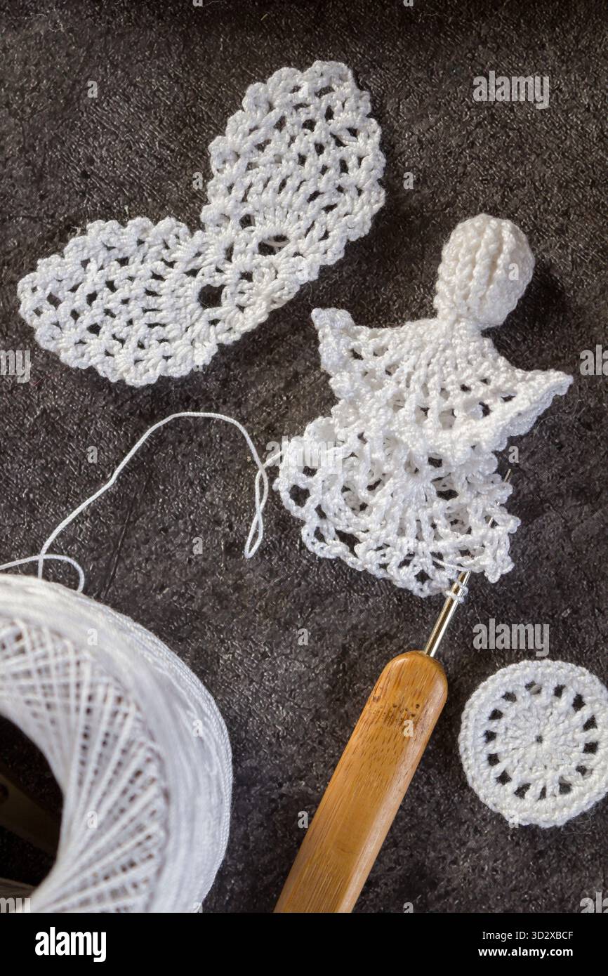 Nahaufnahme eines handgemachten weißen Weihnachtsengels, der mit einer Häkelnadel gemacht wird. Weihnachtsbasteln und DIY-Dekorationskonzept. Stockfoto