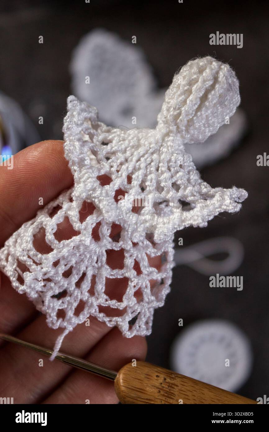 Nahaufnahme eines handgemachten weißen Weihnachtsengels, der mit einer Häkelnadel gemacht wird. Weihnachtsbasteln und DIY-Dekorationskonzept. Stockfoto