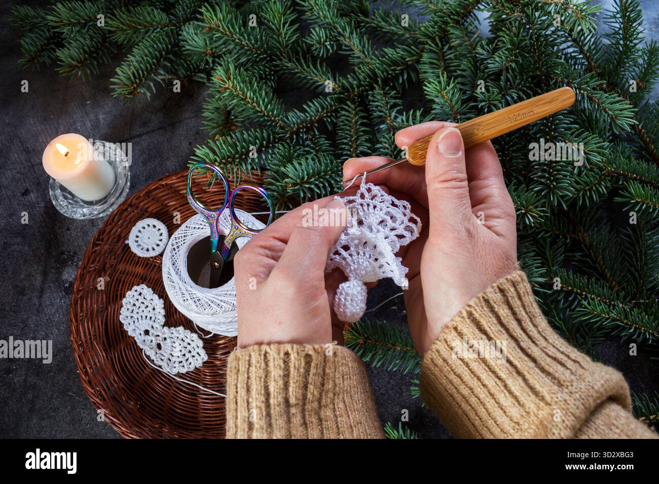 Nahaufnahme eines handgemachten weißen Weihnachtsengels, der mit einer Häkelnadel gemacht wird. Weihnachtsbasteln und DIY-Dekorationskonzept. Stockfoto