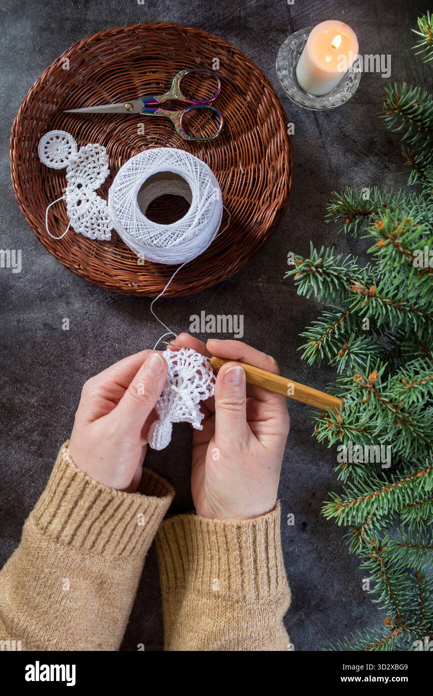 Nahaufnahme eines handgemachten weißen Weihnachtsengels, der mit einer Häkelnadel gemacht wird. Weihnachtsbasteln und DIY-Dekorationskonzept. Stockfoto