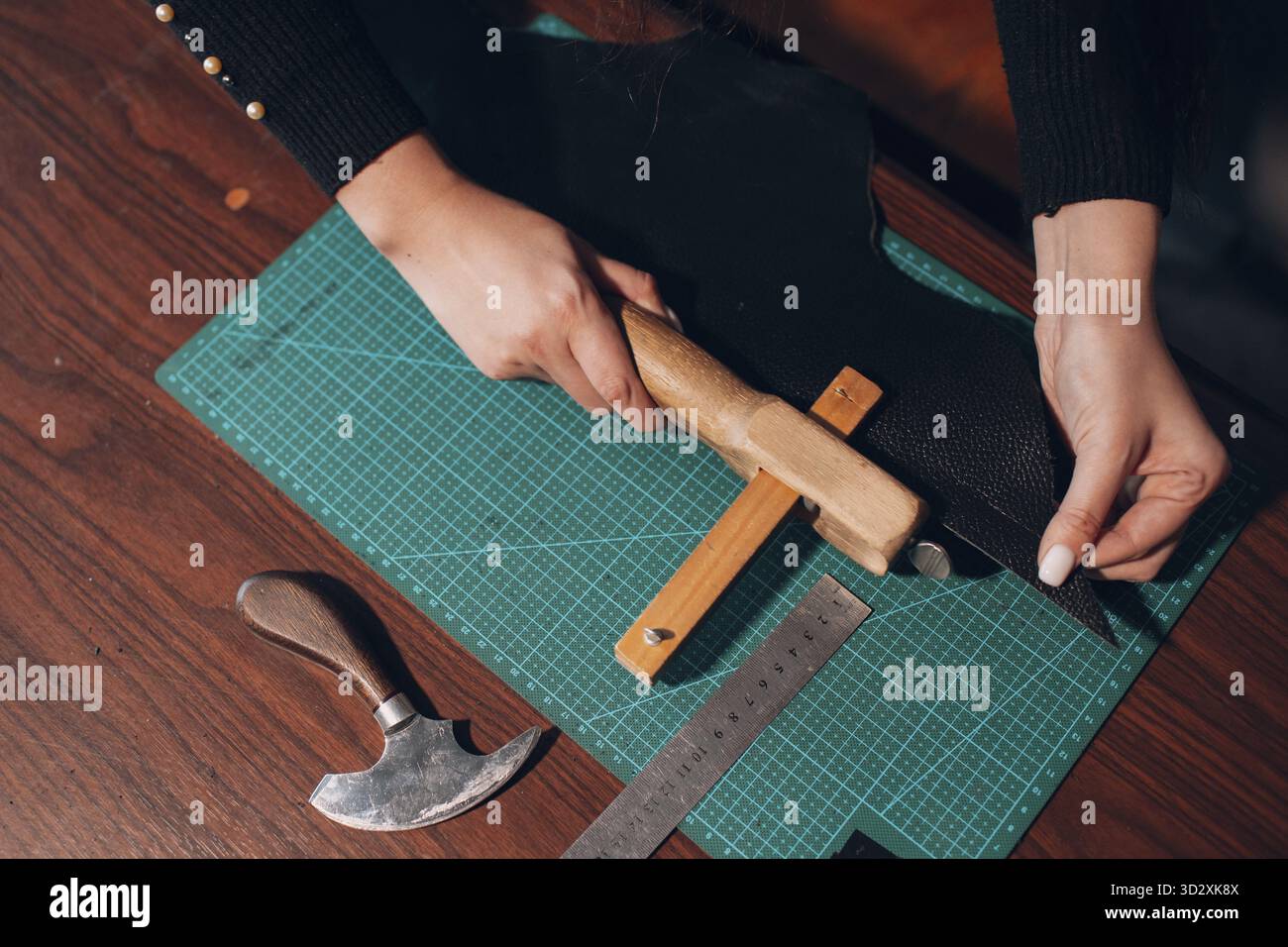 Tanner Frau schneidet Lederwaren in der Werkstatt. Arbeitsprozess des Lederhandwerks Stockfoto