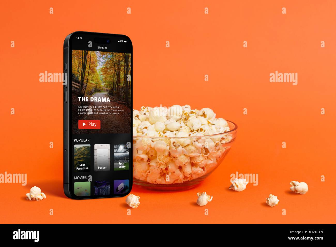 Kinokonzept mit Popcorn, das in eine Glasschale auf orangefarbenem Hintergrund fällt und Spaß, Snacks und Filmunterhaltung in einem minimalistischen stu symbolisiert Stockfoto