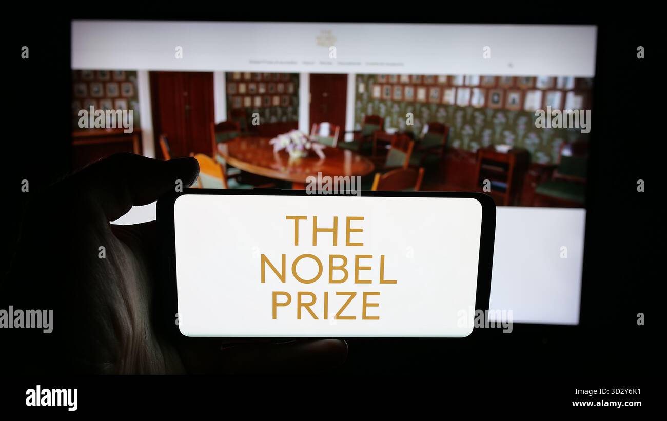 Stuttgart, Deutschland - 10-30-2025: Person mit Mobiltelefon mit dem Logo der Nobelpreise auf dem Bildschirm vor der Webseite. Schwerpunkt auf dem Display des Telefons. Stockfoto