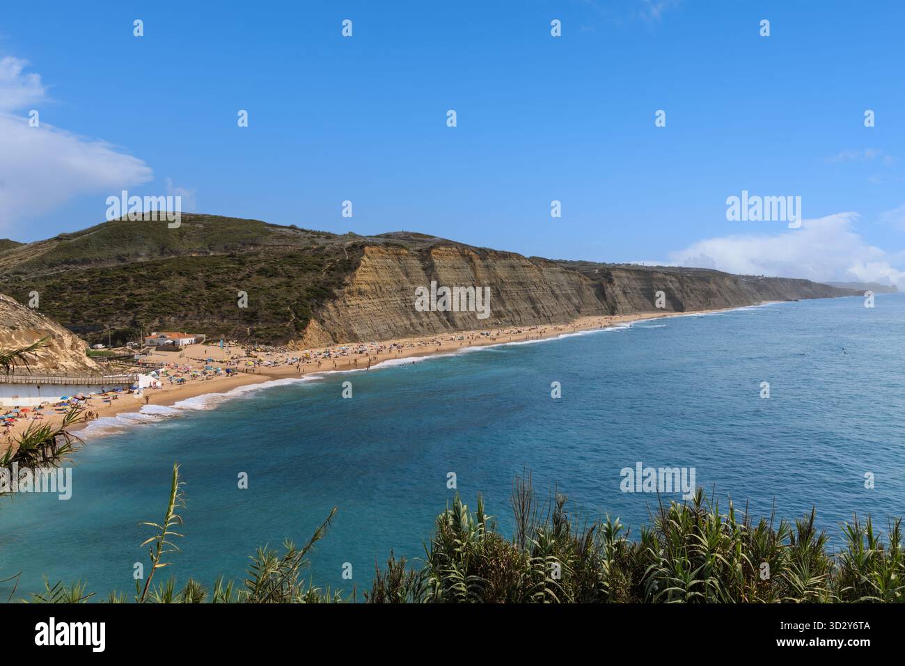 Atemberaubender Panoramablick auf den Strand von Magoito in Portugal, mit dem riesigen Atlantik, goldenem Sand und dramatischen, geschichteten Klippen unter einem klaren Blau Stockfoto