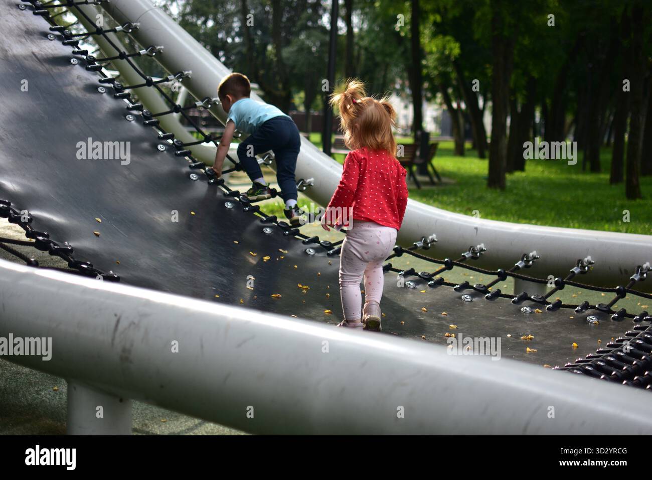 Zwei kleine Kinder klettern auf großen flexiblen schwarzen Netzgeräten im Park im Freien, aktive Bewegung, Teamarbeit, die gemeinsame Bauten in na erkunden Stockfoto