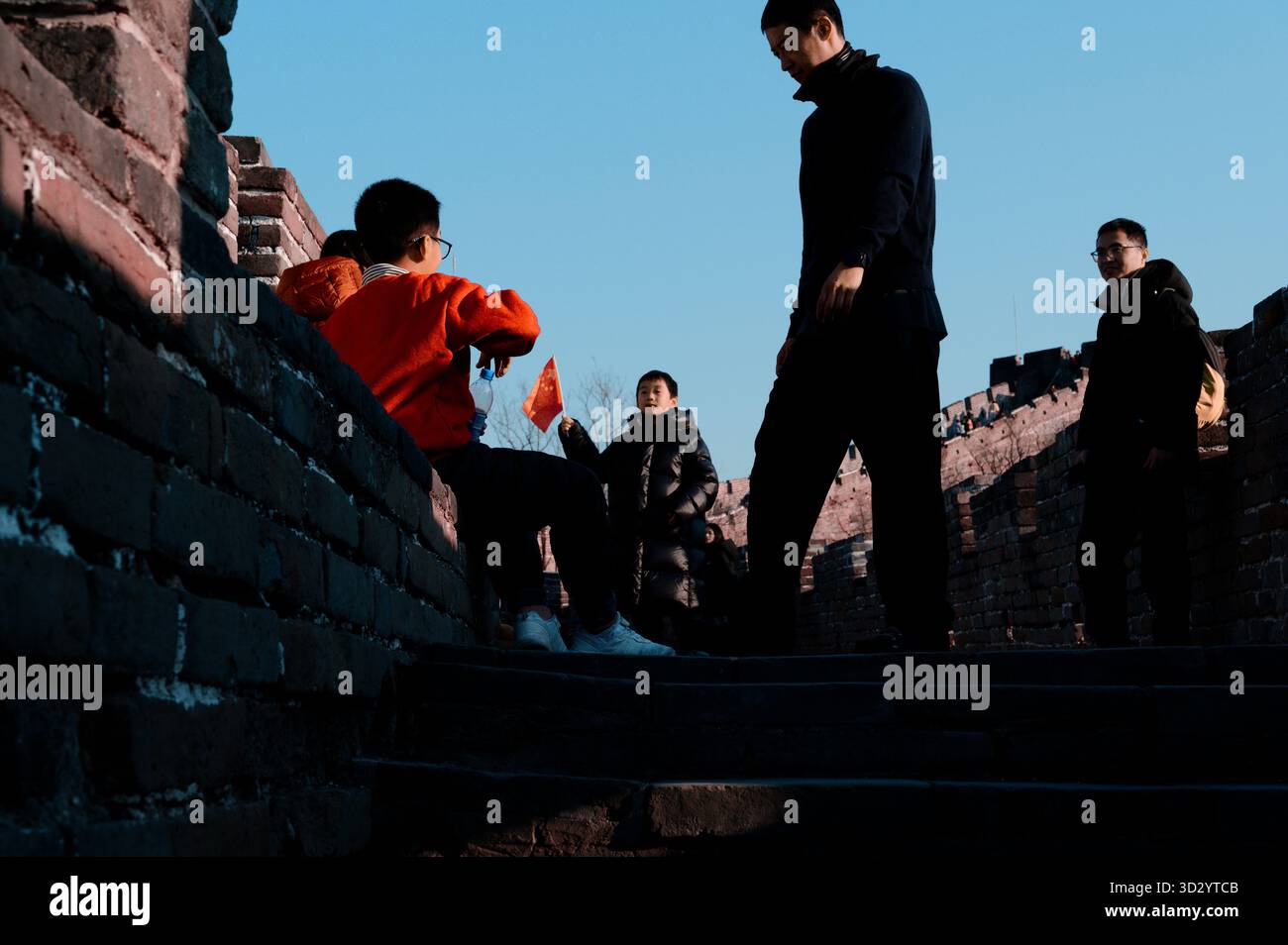 Einheimische Kinder sitzen an der chinesischen Mauer und hängen herum, während man mit chinesischen Fahnen schwingt Stockfoto