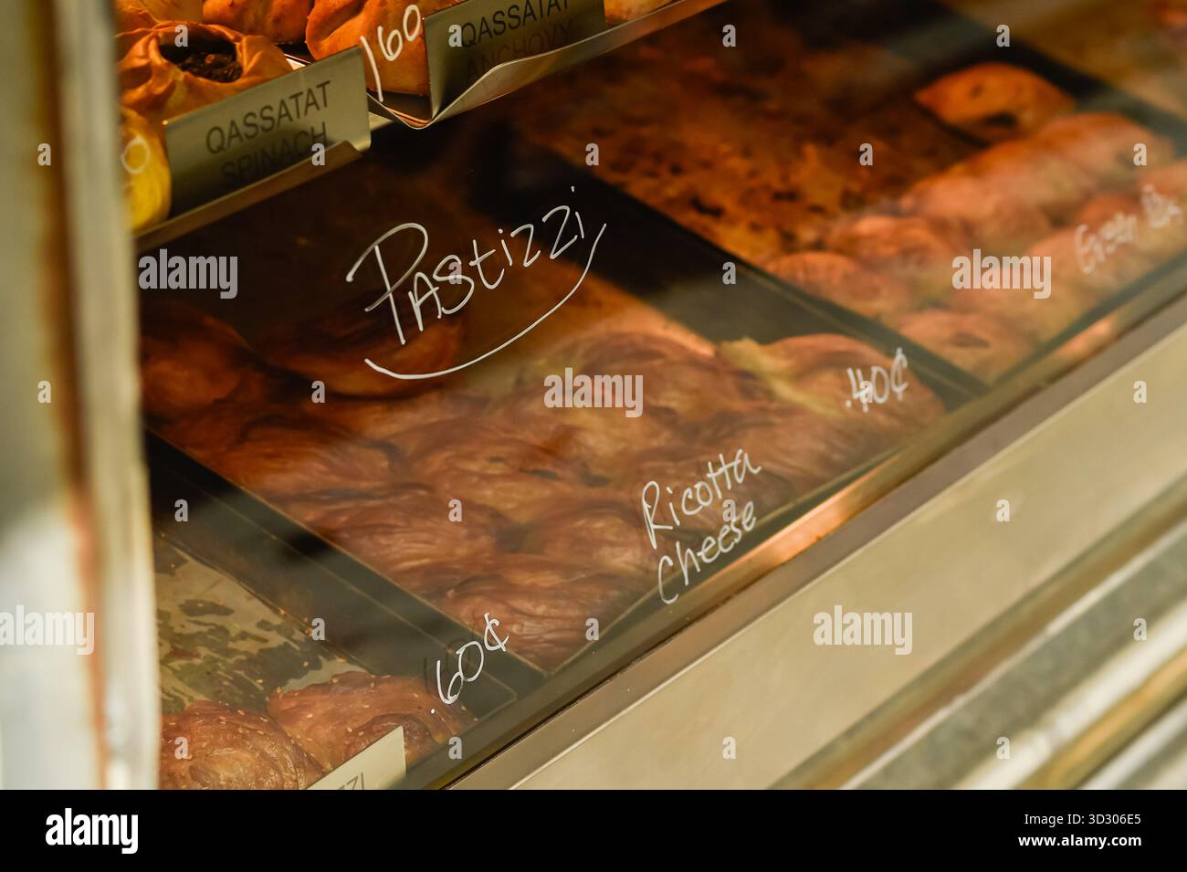 Eine Nahaufnahme frisch gebackener Pastizzi mit Ricotta-Käse-Füllung, deutlich beschriftet in einer warm beleuchteten Glasbäckerei-Vitrine. Konzentrieren Sie sich auf die blättrige Textur des traditionellen maltesischen Gebäckstücks. Stockfoto