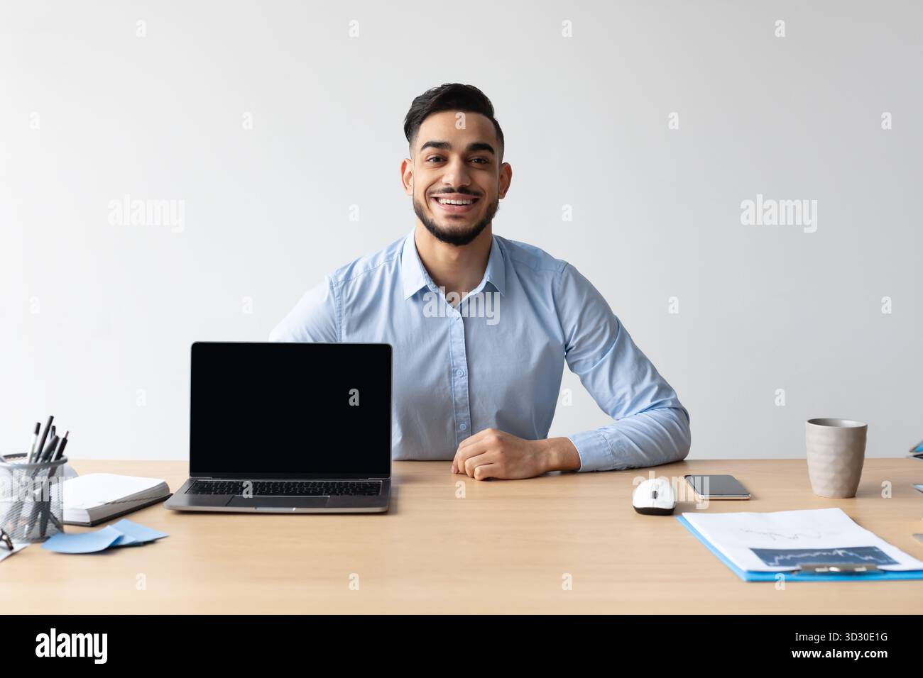 Glücklicher arabischer Mann, der Laptop mit leerem Bildschirm im modernen Home Office-Setup zeigt Stockfoto