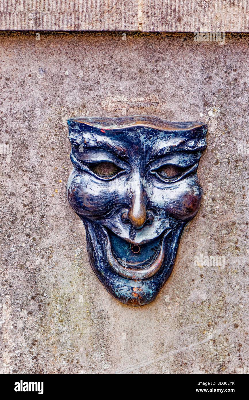 EDINBURGH, SCHOTTLAND - 22. August 2024: Eine dramatische Komödie-Maskenskulptur dient als Wasserauslauf an einer historischen Mauer und verbindet theatralische Tradition mit Qu Stockfoto