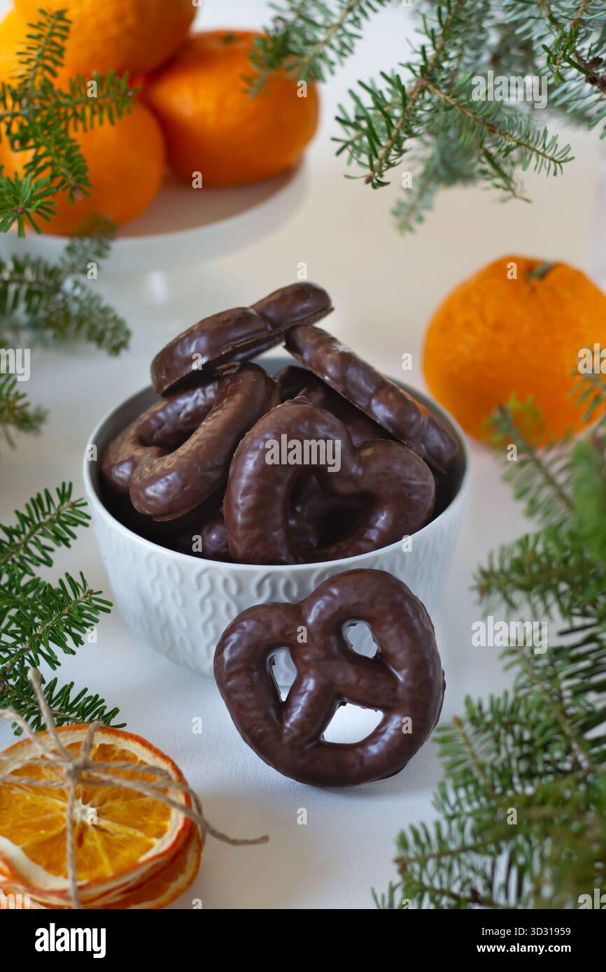 Eine Schüssel mit Brezeln mit Schokoladenüberzug steht auf einem Tisch, dekoriert mit frischen Orangen und grünen Zweigen. Diese Einstellung schafft ein gemütliches festi Stockfoto