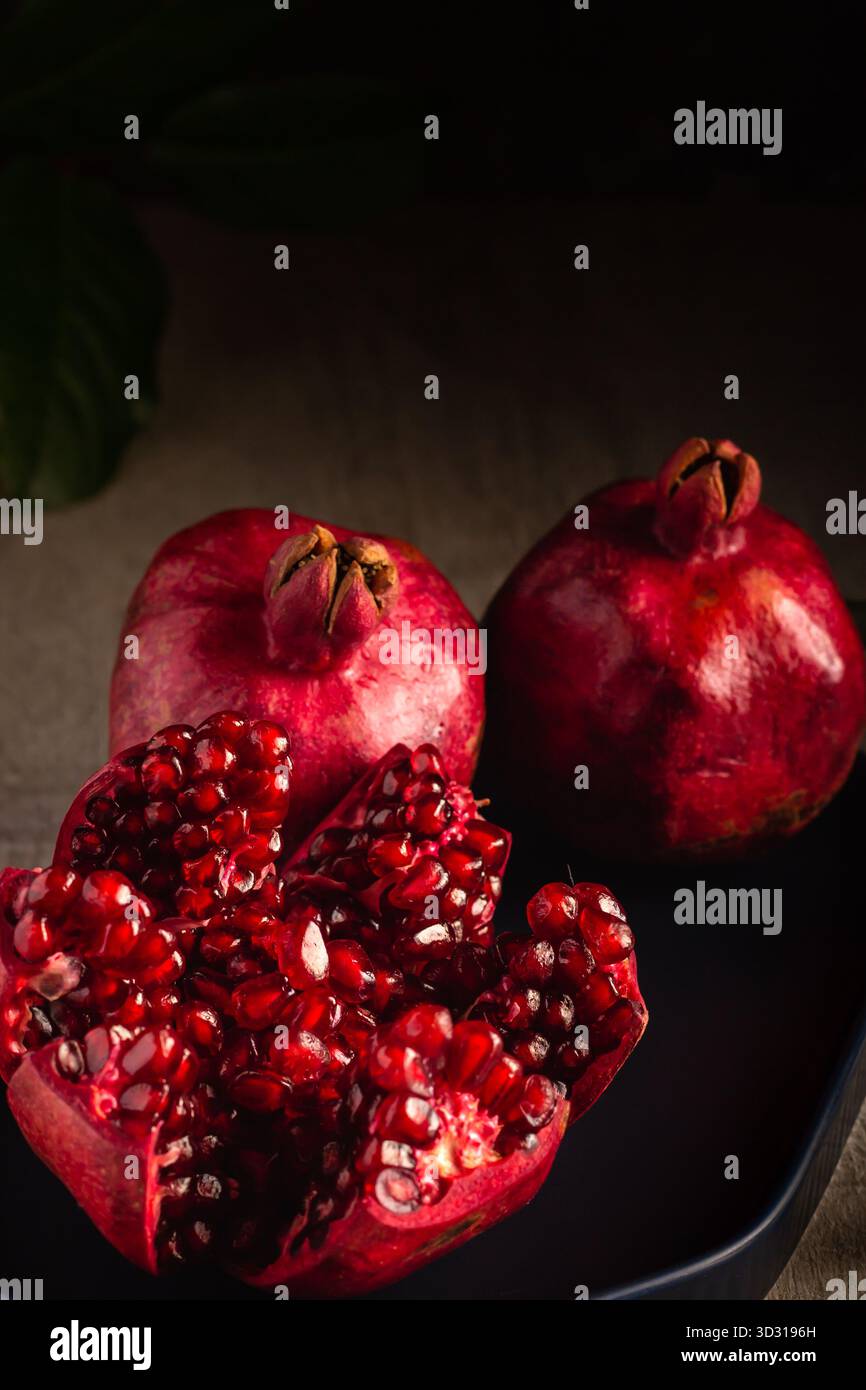 Zwei ganze Granatäpfel sitzen neben einem, der aufgeschnitten wird, und zeigen darin saftige rote Samen. Die Szene ist warm und einladend, perfekt für einen gesunden Snack Stockfoto