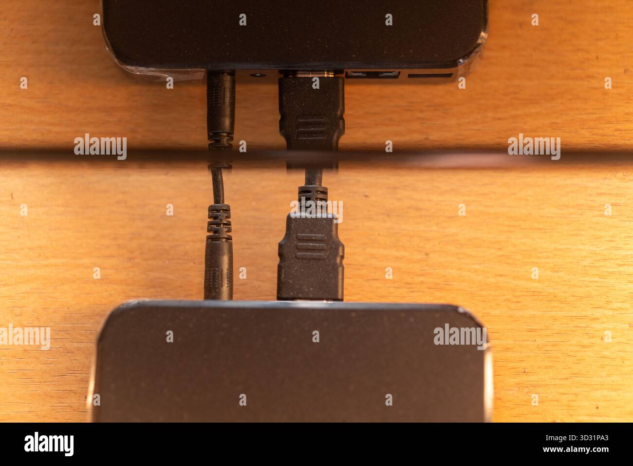 Nahaufnahme von HDMI- und Audiokabeln, die an ein Gerät (Laptop oder Hub) angeschlossen sind. Die Anschlüsse spiegeln sich auf einem glänzenden Holztisch wider. Technologiekonzept. Stockfoto