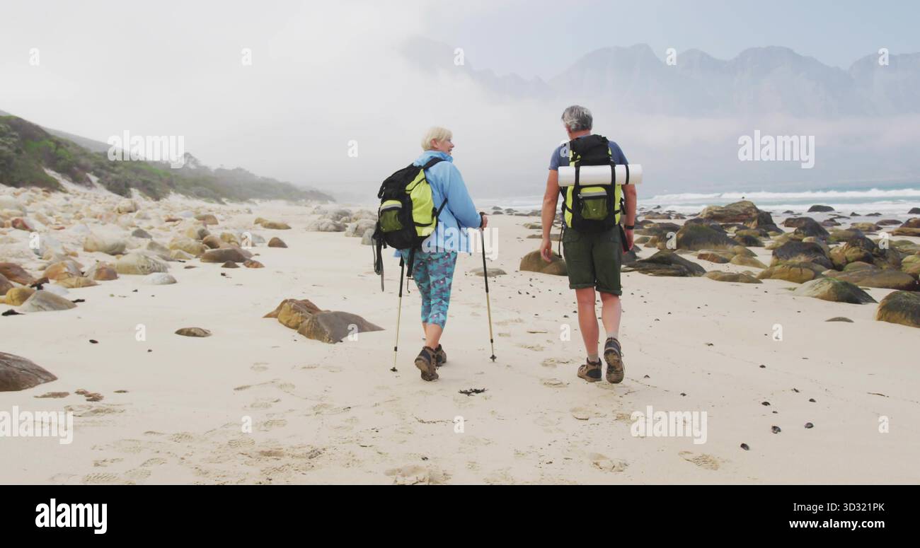 Ein älteres Ehepaar, das die felsige Küste mit Wanderrucksäcken und Trekkingstöcken erkundet Stockfoto