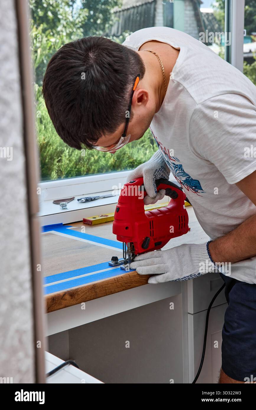 Master mit elektrischer Stichsäge installiert eine moderne Küche, Mann schneidet Loch für das Waschbecken in den Küchenarbeitsplatten, Holzbearbeitung und Tischlerei Konzept Stockfoto