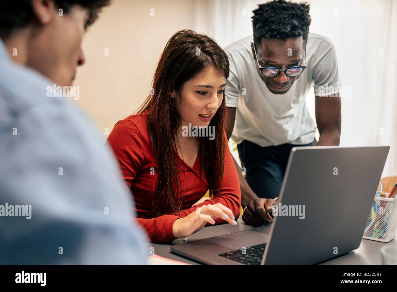 Ein junges multikulturelles Team, darunter ein Schwarzer und eine hispanische Frau, arbeitet an einem Laptop in einer modernen Büroumgebung zusammen. Stockfoto